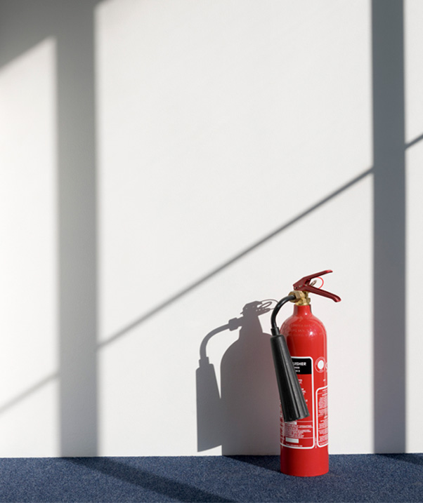 A red fire extinguisher sitting on blue carpet next to a white wall.