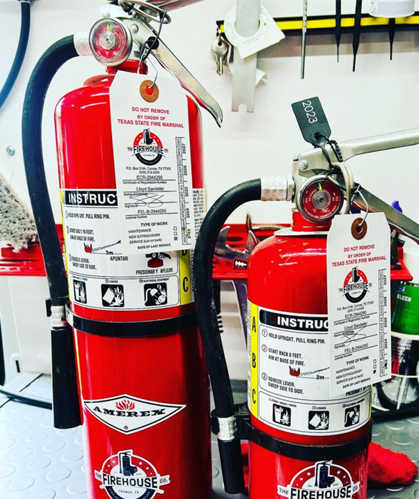 two Amerex fire extinguishers with Firehouse Co. inspection tags sitting in the back of a service van